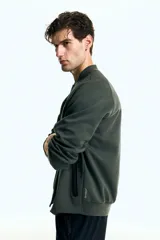 Campera bomber deportiva de tejido funcional color verde oscuro, con cuello elevado corto, cierre bidireccional y mangas raglán. Posee bolsillos delanteros con cierre y costuras selladas.