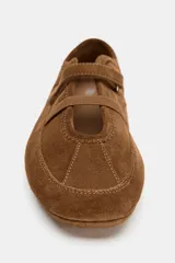 Bailarina deportiva de serraje color marrón, con diseño de doble tira en el empeine, una elástica y otra con cierre adhesivo. Presenta costuras decorativas en el cuerpo, suela plana y punta redonda.