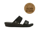 Sandalia plana de cuero negro con dos tiras anchas en el empeine, una de ellas elástica decorada con tachas doradas.