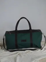 Bolso tipo duffel de gran tamaño, confeccionado en lona color verde oliva con detalles y correas en cuero color suela. Cuenta con cierre superior y etiqueta de cuero con el logo de la marca.
