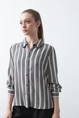 Camisa de manga larga con estampado de rayas verticales en tonos blanco, gris y negro. Presenta cuello clásico con ribete negro y botones frontales negros.