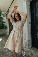 Vestido midi color beige, con cuello camisero, mangas cortas, falda acampanada y cinturón con hebilla forrada. Cierre frontal con botones.