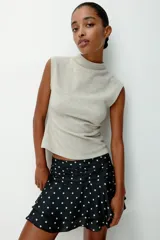 Pollera mini de satén negro con estampado de lunares blancos. Presenta una cintura ancha con pliegues horizontales y un diseño escalonado con volados que aportan volumen y movimiento.