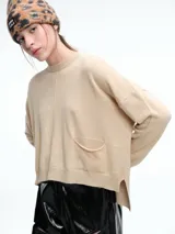 Sweater de tejido de punto color beige, con cuello redondo, hombros caídos y costura central vertical en el frente. Presenta un diseño de corte relajado, con largo asimétrico y aberturas laterales en el ruedo.