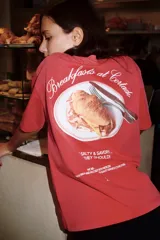 Remera de corte oversize con efecto lavado, color rojo, cuello redondo y manga corta con hombro caído. Presenta un estampado pequeño en el pecho con el logo de la marca y un dibujo lineal de una taza de café.