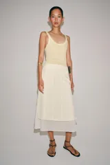 Falda midi de tiro medio, color beige, con detalle de combinación de tejidos a contraste y volante plisado semitransparente en el bajo. Cuenta con cierre lateral de cremallera oculta.