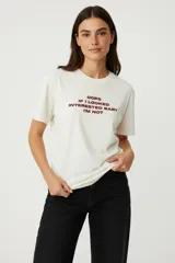 Remera de algodón color crema, manga corta y cuello redondo, con estampado frontal en color bordó que dice "Oops if I looked interested baby I'm not".