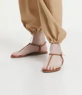 Sandalia plana de mujer color dorado metalizado, con diseño minimalista de tira fina que une la puntera y el empeine, y tira elástica fina alrededor del tobillo.