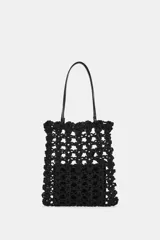 Bolso tipo shopper pequeño de crochet negro, con asas de hombro de material liso negro y una bolsa interior con cierre de cremallera.