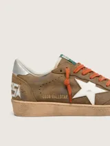 Zapatillas Golden Goose modelo Ball Star, confeccionadas en gamuza encerada marrón con efecto vintage. Tienen estrella lateral blanca, cordones naranjas, contrafuerte plateado en el talón y suela de goma con acabado envejecido.