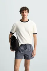 Bañador largo de hombre color rosa pálido con textura seersucker. Presenta cintura elástica ajustable con cordón blanco, bolsillos laterales y un bolsillo trasero de plastrón.