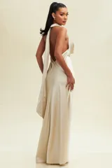 Vestido largo de satén color beige, con escote halter y espalda descubierta. Presenta un diseño minimalista con corte fluido y acabado brillante.