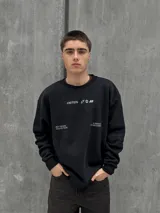 Buzo negro de corte holgado con cuello redondo y puños acanalados. Estampado frontal con la palabra "OSTEN" y la frase "NOT WHERE YOU'RE FROM A MINDSET OF BECOMING" en color blanco.