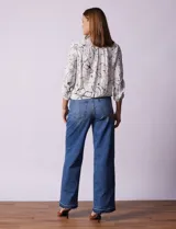 Blusa blanca estampada con flores negras, cuello redondo, abertura con botones y mangas 3/4 con frunce. Tiene terminación con nudo en el ruedo.