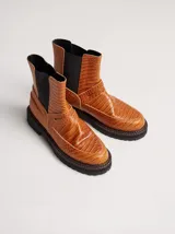 Bota de cuero color tostado con textura símil cocodrilo, diseño tipo Chelsea con elásticos laterales negros, costuras pespunteadas y suela dentada de goma.