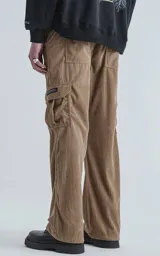 Pantalón cargo de corderoy color arcilla (marrón claro/beige), de calce regular y tiro alto con elástico fruncido. Presenta seis bolsillos, incluyendo dos bolsillos cargo con solapa en las piernas.