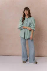 Camisa de denim color verde menta con calce relajado, cuello clásico, cierre frontal con broches metálicos, mangas largas y bolsillo aplicado en el pecho, con detalles en tono gris azulado a contraste en cuello, cartera, bolsillo y puños.