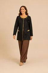 Chaqueta larga negra de corte recto, con bordados dorados en el cuello y bordes frontales. Presenta aplicaciones de flores negras con tallos dorados en el lateral derecho y detalles bordados en los bolsillos. Diseño artesanal elegante.