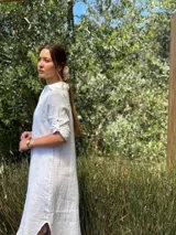 Vestido camisero largo de lino blanco, con cuello camisero, manga corta enrollada y cierre frontal de botones de nácar. Presenta aberturas laterales en el bajo.