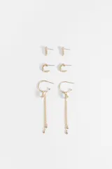 Set de tres pares de aros dorados con apliques de vidrio transparente. Incluye un par de aros pequeños tipo botón con diseño rectangular, un par de aros pequeños en forma de argolla con pedrería y un par de aros tipo argolla con dijes colgantes de estrella y cadenas finas con detalles de cristal.