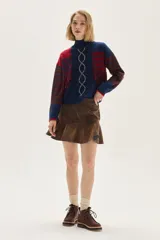 Polera de tejido de punto con diseño multicolor que combina rayas horizontales, trenzas verticales y flecos decorativos. Presenta cuello semi polera, mangas largas con bordado y puños acanalados.