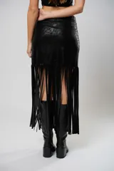 Pollera midi de cuero sintético negro, con diseño de tajo lateral y ruedo decorado con flecos largos que aportan movimiento.