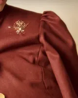 Chaqueta de paño color bordó, de cuello mao y mangas abullonadas en los hombros. Presenta un detalle bordado de cuentas y canutillos dorados en el pecho.