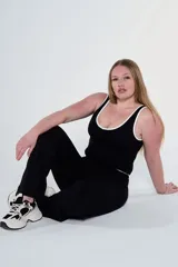 Conjunto deportivo compuesto por una musculosa negra con ribetes blancos en cuello y sisas, y un pantalón largo negro de corte recto. El diseño es ajustado y versátil, ideal para actividades físicas o uso casual.