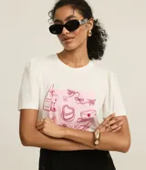 Remera blanca de algodón con cuello redondo y mangas cortas abullonadas. Presenta un estampado con dibujos de objetos femeninos en tonos rosados.