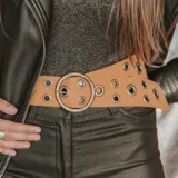 Cinto ancho color camel con hebilla circular plateada y ojales metálicos.