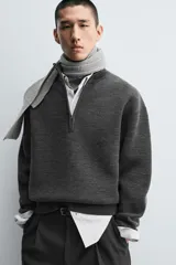 Jersey de punto de corte regular, color gris oscuro, con cuello subido y cierre frontal de cremallera. Presenta mangas largas y acabados en rib en puños y ruedo.