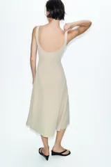 Vestido midi de color beige con escote cuadrado y tirantes anchos. Presenta un diseño entallado en el torso con costuras verticales marcadas y una falda con caída evasé.