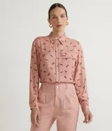 Camisa de viscosa color rosa con estampado de caballos en marrón. Tiene cuello camisero, cierre con botones, mangas largas, un bolsillo frontal y detalle de vivo contrastante en el bolsillo.