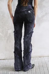 Pantalón de jean con lavado efecto violeta, de corte entallado y botamanga acampanada. Presenta recortes irregulares con costuras desflecadas a lo largo de las piernas y cintura de tiro alto.