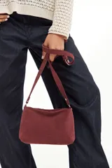 Bandolera pequeña de cuero gamuzado color bordó, con correa larga regulable y cierre superior.