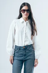 Camisa blanca de manga larga con diseño de rayas verticales sutiles en la misma tela. Presenta cuello clásico, cierre frontal con botones y mangas abullonadas con puños elásticos.