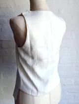 Chaleco blanco sin mangas, con escote en V profundo y cierre frontal mediante lazos anudados.