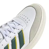 Championes urbanos Adidas modelo Urban Courtblock, de color blanco con detalles en verde oscuro, amarillo y gris. Presentan un diseño de inspiración tenística con puntera reforzada en gamuza gris, las icónicas tres tiras laterales en verde con bordes amarillos y el logo de la marca en la lengüeta.