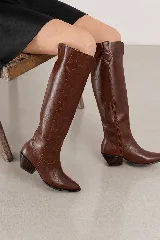 Bota de caña alta confeccionada en cuero genuino color marrón, con diseño de inspiración western, taco cuadrado bajo y punta fina.
