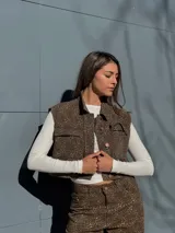 Chaleco corto con estampado animal print marrón y negro, cuello camisero, cierre frontal con botones y bolsillos de parche en el pecho.