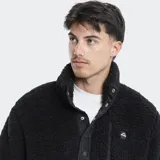 Campera de polar tipo borreguito color verde oliva, con cuello alto, cierre frontal parcial con botones a presión y bolsillo en el pecho con cierre. Presenta detalles en color beige en la solapa y los bordes.
