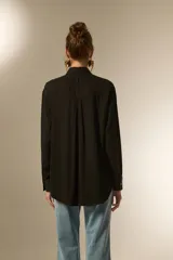 Camisa negra de viscosa con corte holgado, cuello clásico, cierre frontal de botones y detalle de tachas metálicas en la línea de los hombros.