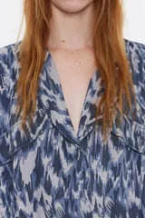 Mono largo de viscosa con estampado abstracto en tonos azules y grises. Tiene cuello camisero con solapa, manga corta murciélago con fruncidos en los hombros, cierre frontal con cremallera oculta, bolsillos con tapeta redondeada en el pecho y con fuelle en la cadera, y cinturón de tela.