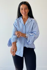 Camisa de mangas largas con diseño de rayas verticales en tonos celeste y rosa. Presenta cuello clásico, cierre frontal con botones y puños con volados.