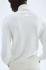 Polera blanca de punto fino, con cuello alto, mangas largas y bajo recto. Cuello, puños y bajo acanalados.