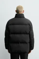 Cazadora acolchada de corte relajado confeccionada en tejido técnico color verde militar. Presenta cuello subido, cierre frontal con cremallera, mangas largas con puños elásticos y bolsillos frontales con cremallera oculta.