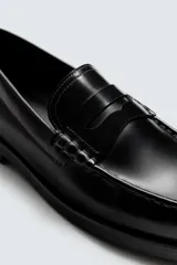 Mocasín de vestir tipo penny loafer, fabricado en piel con acabado brillante, horma redonda y suela con ligero tacón.