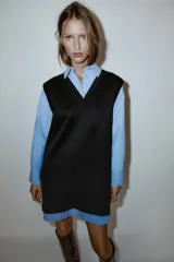Vestido corto que combina una camisa celeste de manga larga con cuello solapa y botones frontales, con un chaleco de tejido negro sin mangas y escote en V superpuesto.