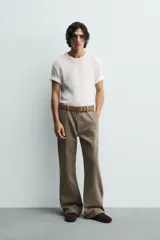 Pantalón de denim color verde oliva, estilo chino con corte ancho y bota acampanada (flare) desde la rodilla. Tiro medio, confeccionado en tejido rígido. Presenta bolsillos frontales y bolsillos traseros de plastrón.