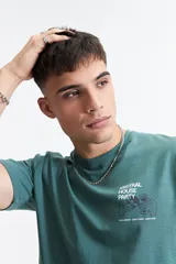 Remera de manga corta color verde azulado, con escote redondo y fit regular. Presenta un estampado gráfico en la espalda con texto "MISTRAL HOUSE PARTY 9/03" y un diseño de manos sosteniendo copas de vino y un disco de vinilo.